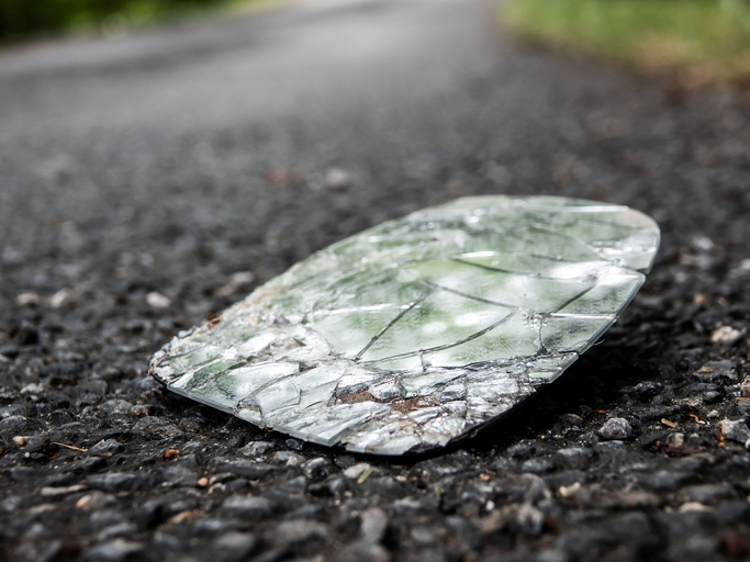 Broken shards of the rearview mirror of the car on an asphalt road